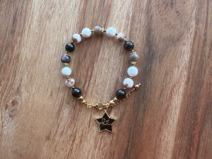 Pulseira feminina artesanal com cristais naturais Turmalina Negra, Pedra do Sol Negra, Jade, Magnesite e Hematite. Inclui pendente estrela ou coração com a palavra “Fé”. Criação com intenção para proteção, serenidade e equilíbrio emocional.