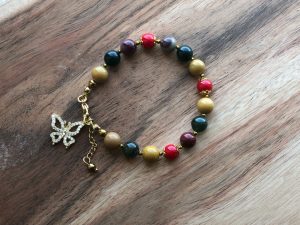 Pulseira feminina artesanal com cristais Jaspe Mookaite, Coral Vermelho, Ágata Musgo e Hematite. Inclui pendente borboleta com zircónias brancas. Criação com intenção para ação consciente, renovação interior e estabilidade emocional.